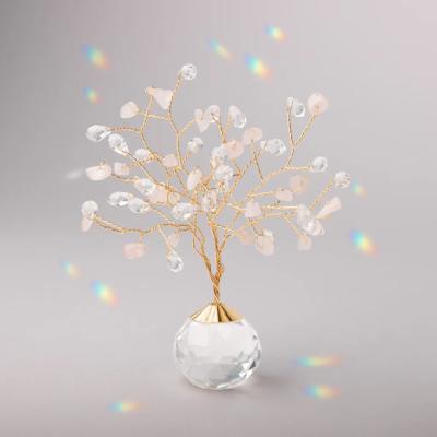 Gold wire gemstone tree with clear and blush crystals in a faceted glass base on a gray background