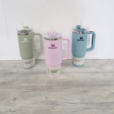 Set of three pastel Stanley handled tumblers with straws in green, pink, and blue on a wood surface