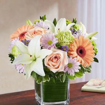 Mixed bouquet of lilies, roses, and daisies in a square glass vase