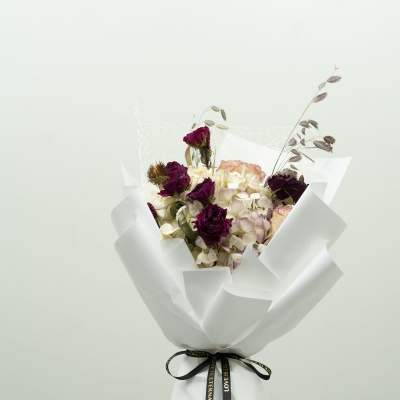 Bouquet of dark purple roses and pale hydrangeas wrapped in white paper