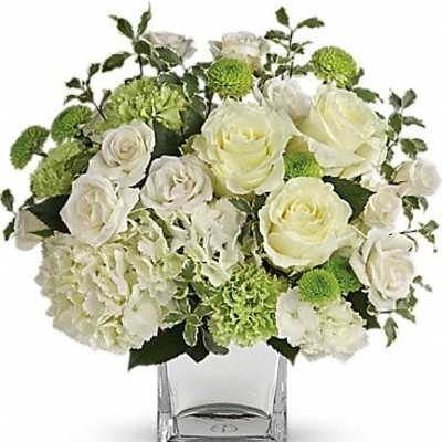 White roses and green pom flowers in a clear square vase