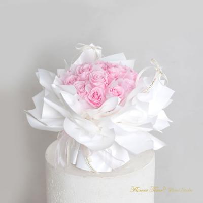 Pink rose bouquet wrapped in white paper on a white pedestal
