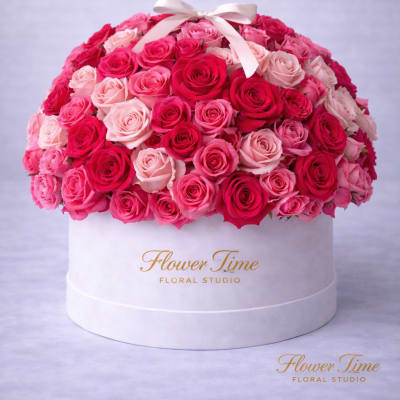 Round box arrangement of pink and red roses with a white ribbon bow