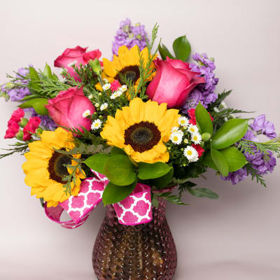 Bouquet of sunflowers, pink roses, and purple flowers in a glass vase
