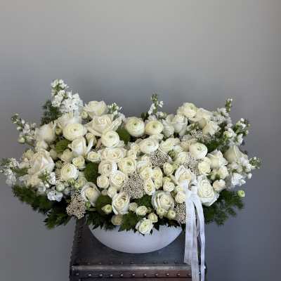 Large white rose arrangement in a low white bowl with trailing ribbon