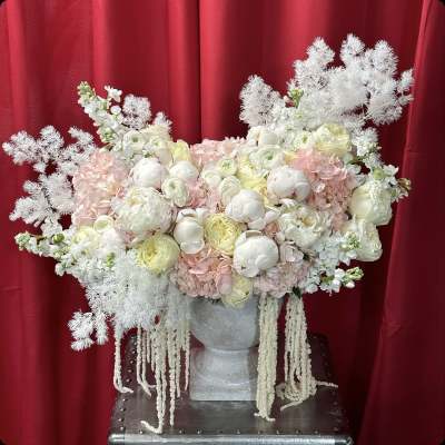 Large pastel floral arrangement in a silver vase against a red backdrop