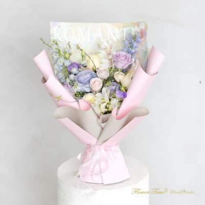 Pastel bouquet of roses, lilies, and blue flowers wrapped in pink paper