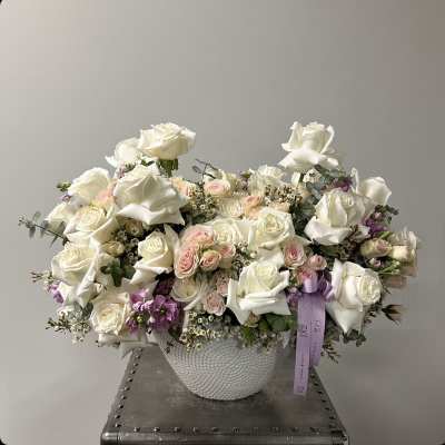 White rose arrangement in a textured white vase with a lavender ribbon