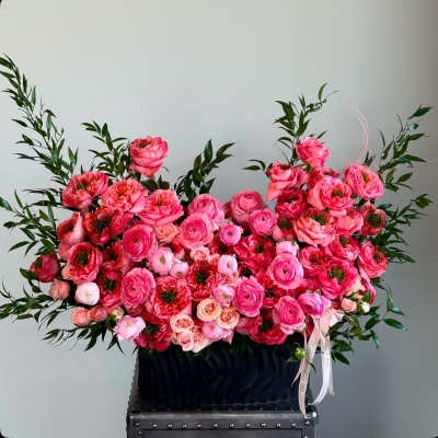 Large pink floral arrangement in a black container with ribbon