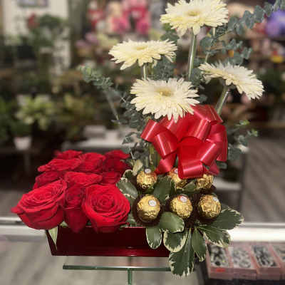 Rectangular arrangement with red roses, pale gerbera daisies, red bow, and gold-wrapped chocolates