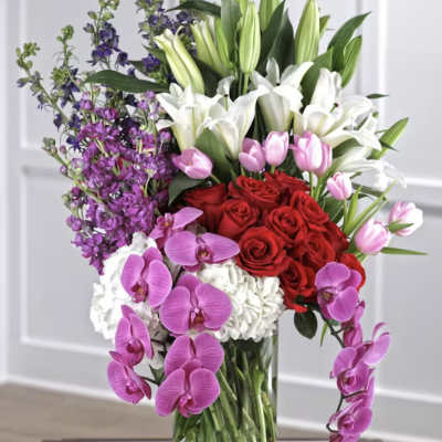 Tall bouquet of red roses, white lilies, pink tulips, and purple orchids in a glass vase