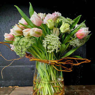 Pink and white tulips arranged in a glass vase with curly branches