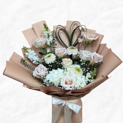 Bouquet of pale roses and white blooms wrapped in tan paper with a ribbon