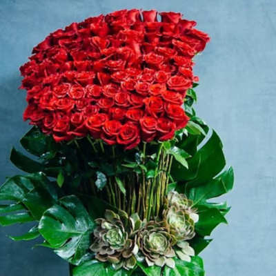 Large red rose arrangement in a tall green vase with succulents