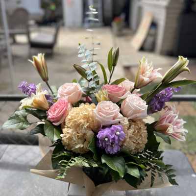 Mixed bouquet of pink roses, lilies, and purple blooms in a box