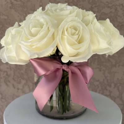 White rose bouquet in a glass vase with a pink ribbon