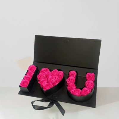 Pink roses arranged in an open black box spelling "I ♥ U"