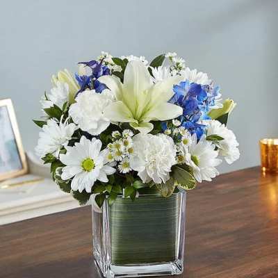 White and blue mixed flower arrangement in a square glass vase