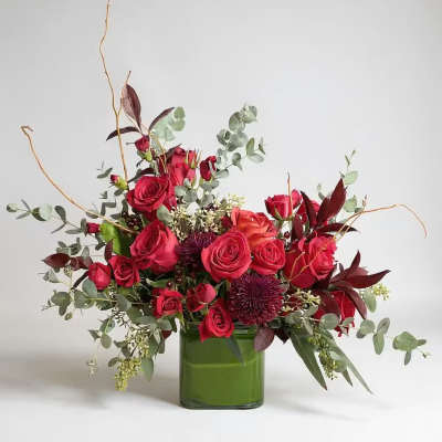 Red roses arranged in a green glass vase with airy foliage