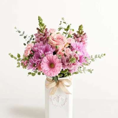 Pink and lavender flower arrangement in a white ceramic vase with a bow