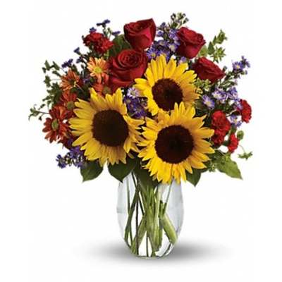 Bouquet of sunflowers, red roses, and mixed daisies in a clear glass vase