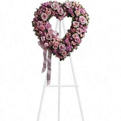 Heart-shaped pink rose wreath on a white stand with ribbon