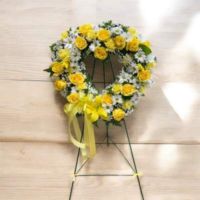Yellow roses and white daisies arranged in a heart-shaped wreath on a stand.