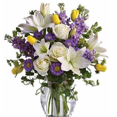 Bouquet of white lilies, roses, and purple flowers in a glass vase