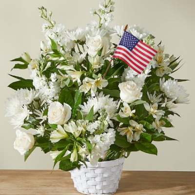 White floral arrangement in a white basket with a small American flag