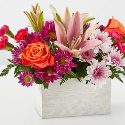 Rectangular arrangement of pink lilies, orange roses, and purple and white daisies in a white box.