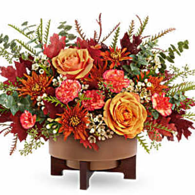 Autumn floral arrangement with orange roses and red blooms in a low container