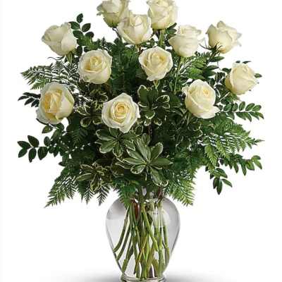 White roses arranged in a clear glass vase with mixed greenery