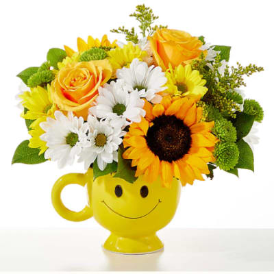 Yellow mug vase with a smiley face holding yellow and white flowers