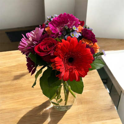 Bright mixed bouquet of gerbera daisies and roses in a clear glass vase