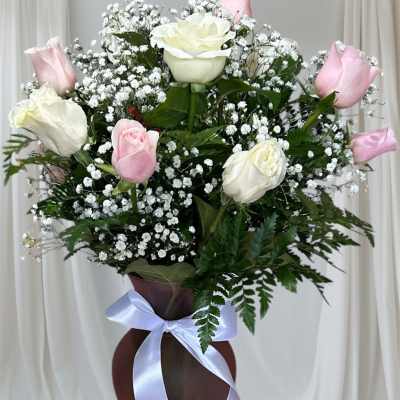 Pink and white roses arranged in a tall vase with baby's breath