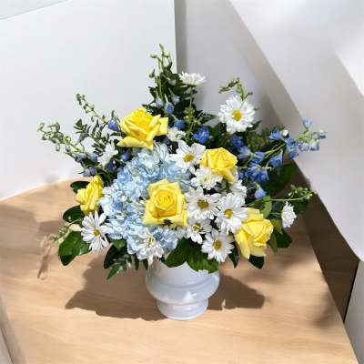 Yellow roses and white daisies in a white vase with blue flowers