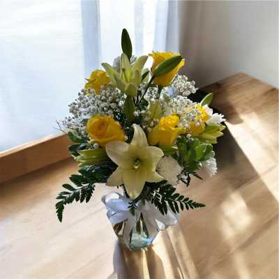 Yellow lilies and roses in a glass vase with a white ribbon