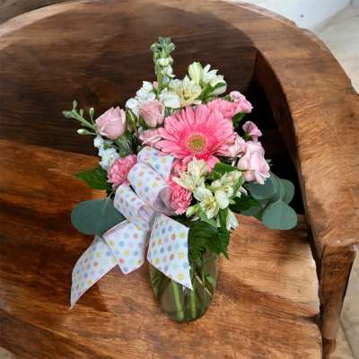 Mixed pink and white flower arrangement with bow in a clear vase on a wooden chair