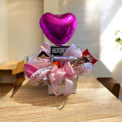 Heart-shaped pink balloon above a candy gift basket with a pink bow