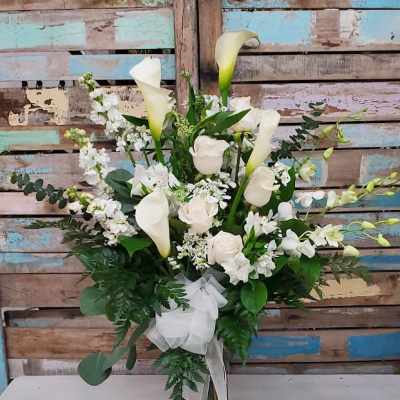 White calla lilies and roses in a tall vase with a white ribbon