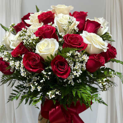 Red and white roses arranged in a glass vase with a red ribbon