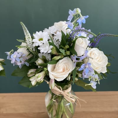 White roses and blue flowers arranged in a glass vase