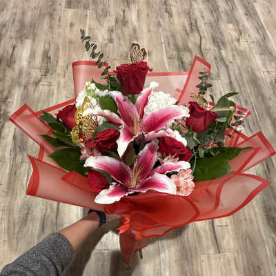 Handheld bouquet of red roses and pink lilies wrapped in red paper