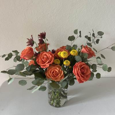 Orange roses and yellow button mums in a clear glass vase