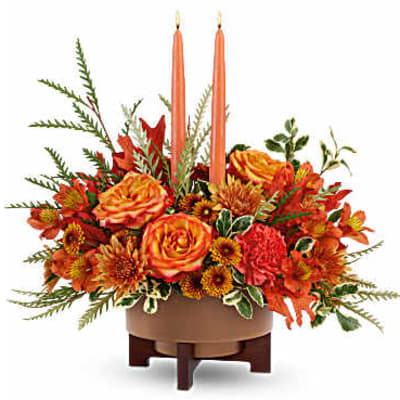 Orange floral centerpiece with two tall taper candles in a low bowl