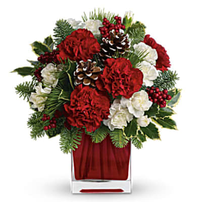 Red and white floral arrangement in a clear square vase with pinecones and berries