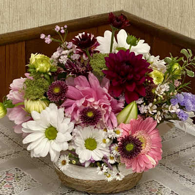 Mixed bouquet of pink, white, and burgundy flowers in a woven basket