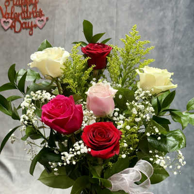Bouquet of red, pink, and white roses in a silver vase with a white ribbon