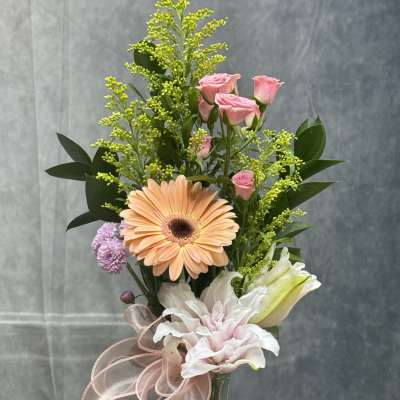 Mixed bouquet in a glass vase with pink roses, a peach gerbera, and white lilies