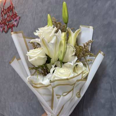 White roses and lilies in wrapped bouquet with gold ribbon